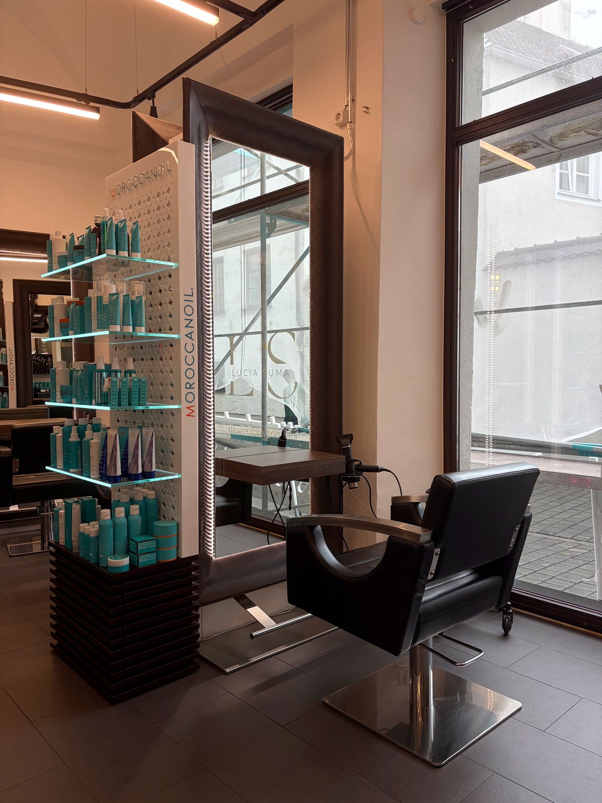 Stylingplatz am Schaufenster im Haarstudio Galerie da Lucia: großer LED-Spiegel mit Schriftzug Lucia Suma und Moroccanoil-Produktregal