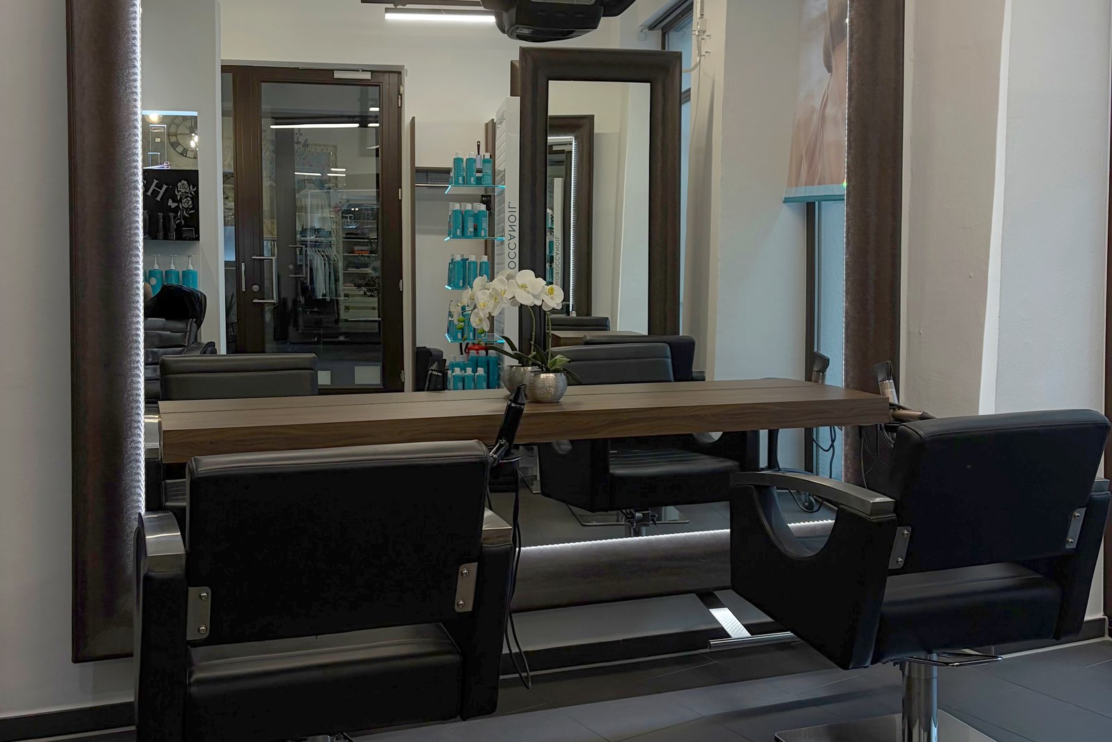 Stylingplatz im Haarstudio Galerie da Lucia: großer beleuchteter Spiegel, Holztresen mit Orchidee und schwarze Friseurstühle